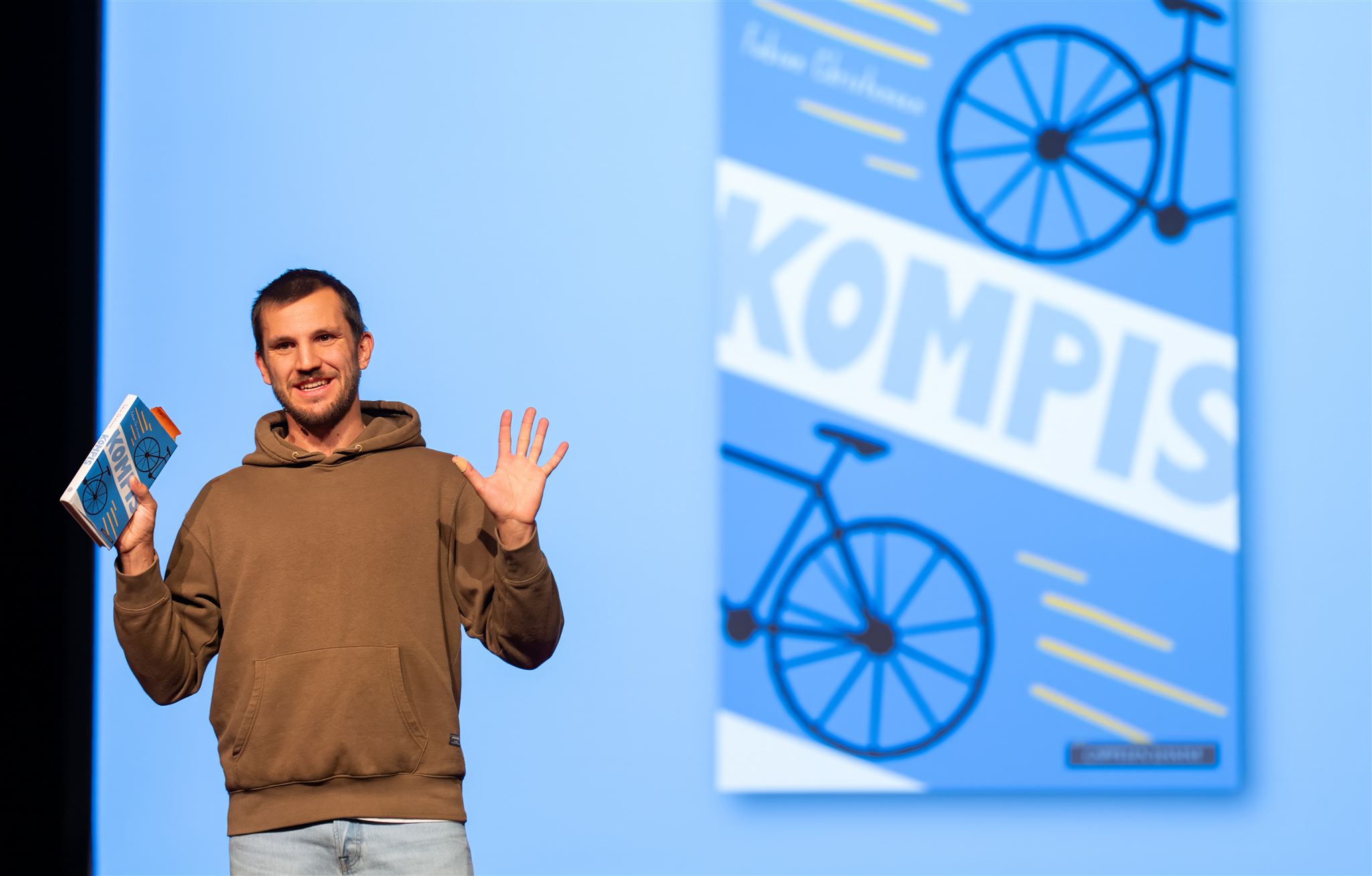 Fabian Christensen med bok i hånda, foran storskjerm med bilde av den samme boka.