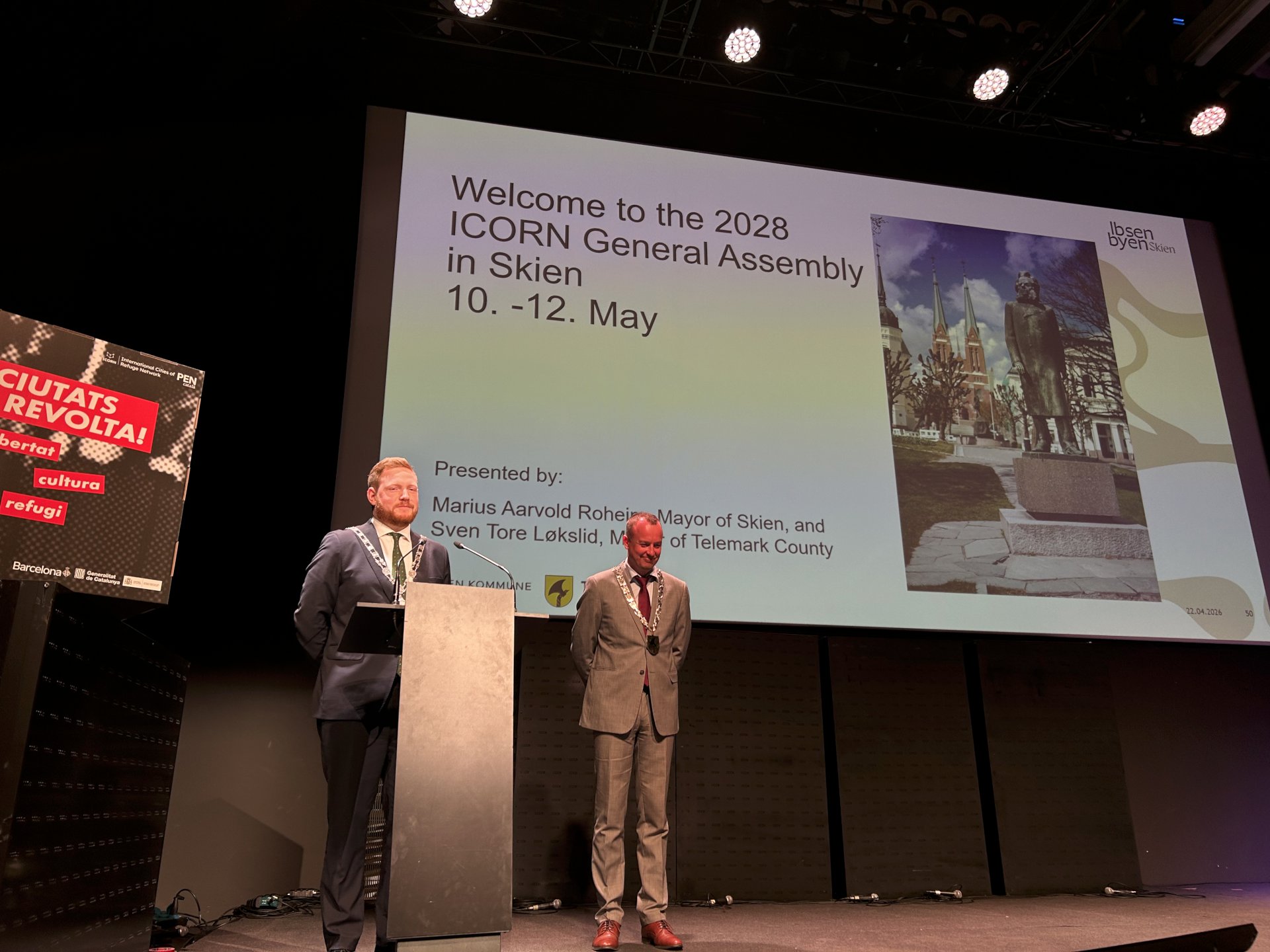 To menn står på en scene og snakker.